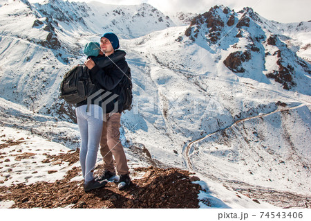 A young man hugs his wife on a background of snowy mountains. Holidays in the mountains. A young man hugs his wife on a background of snowy mountains. Holidays in the mountains. 74543406