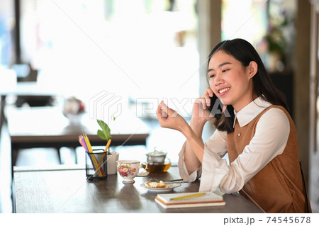 Cheerful young woman talking on mobile phone while siting in modern coffee shop. 74545678