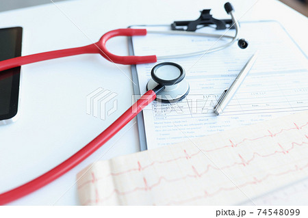 Stethoscope and electrocardiogram lying on patients medical history closeup Stethoscope and electrocardiogram lying on patients medical history closeup 74548099