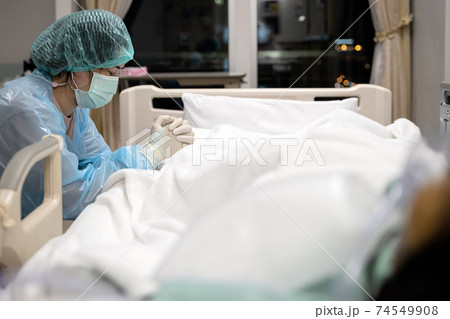 Sad asian woman or nurse in face mask and medical uniform,pray with closed eyes,hands clasped together,say a prayer for senior patient lying in the hospital bed,take care,look after of the old elderly 74549908