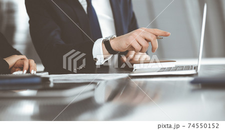 Unknown businessmen and woman sitting, using laptop computer and discussing questions at meeting in modern office, close-up 74550152