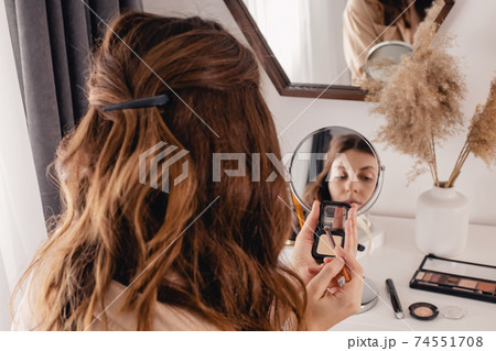 Young woman applying make-up to her face, looking at the round mirror Young woman applying make-up to her face, looking at the round mirror 74551708