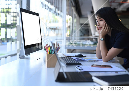 Businesswoman sitting in front of computer at her workspace and thinking about project. Businesswoman sitting in front of computer at her workspace and thinking about project. 74552294