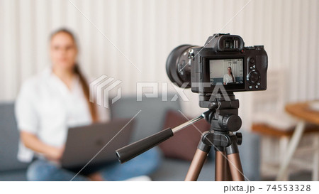 Blogger recording video indoors, selective focus on camera display 74553328