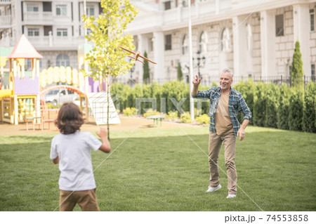 Dad and son playing together on a lawn and looking involved Dad and son playing together on a lawn and looking involved 74553858