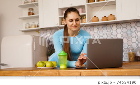 Smiling woman using computer in modern kitchen. Healthy lifestyle concept 74554190
