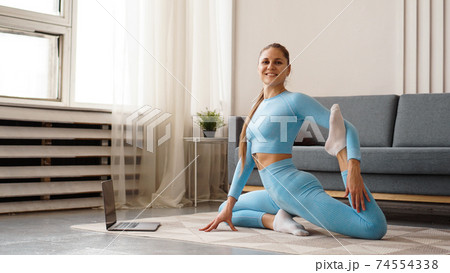 Beautiful young woman doing fitness exercise at home with her laptop Beautiful young woman doing fitness exercise at home with her laptop 74554338