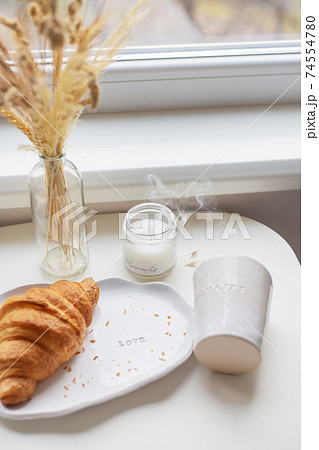 White glass and a plate on which lies a croissant made of clay with the inscription love, handmade. 74554780