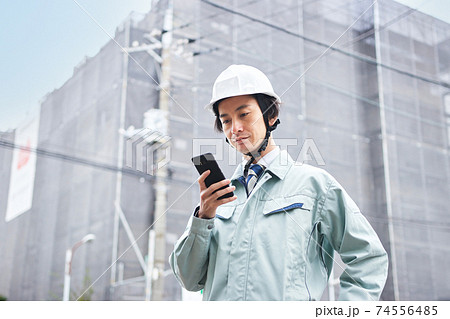建設現場の前でスマホを見る作業服の男性 74556485