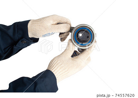 A car locksmith holds a spent old timing belt tensioner roller on a white background, isolate. Timing Belt Roller Replacement Concept 74557620