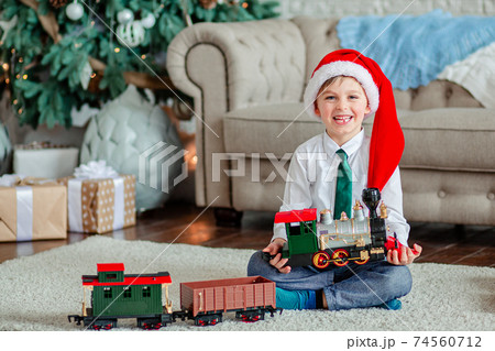 Good morning. Happy little boy with a gift, toy train, under the Christmas tree on New Year's morning. Time to fulfill wishes. 74560712