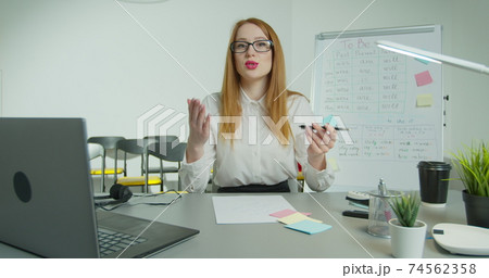 English teacher virtual teaching look at webcam give distance lesson. Female school tutor explain online class talking to camera sit at desk in classroom. Video conference call education. 74562358