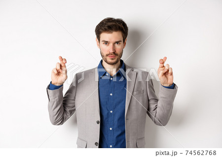 Hopeful man in suit cross fingers for good luck and looking confident in win, feeling determined, standing on white background Hopeful man in suit cross fingers for good luck and looking confident in win, feeling determined, standing on white background 74562768