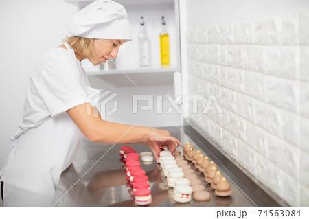 cooking, food and baking concept. Pretty woman confectionery chef making colorful tasty macarons, connect the halves with ganache cream at modern kitchen in pastry shop cooking, food and baking concept. Pretty woman confectionery chef making colorful tasty macarons, connect the halves with ganache cream at modern kitchen in pastry shop 74563084