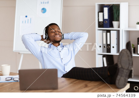 Relaxed black man employee listening to music in his office Relaxed black man employee listening to music in his office 74564339