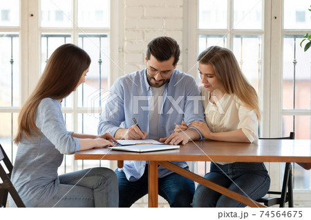 Happy young clients signing paper contract with professional broker. 74564675