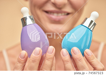 Close up of happy adult woman holding jars of serum to moisturize the skin Close up of happy adult woman holding jars of serum to moisturize the skin 74567323