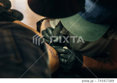 Close up of professional tattooer artist doing picture on hand of man by machine black ink from a jar. Close up of professional tattooer artist doing picture on hand of man by machine black ink from a jar. 74567389
