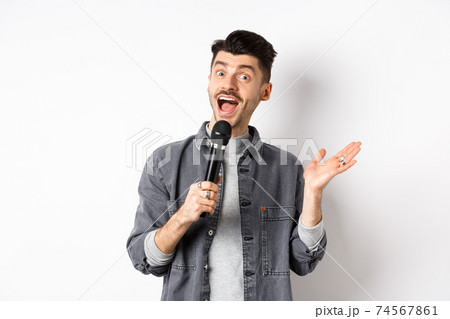 Excited stylish guy giving speech, talking in microphone, perform or sing karaoke, standing on white background 74567861