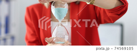 Woman in business suit holding hourglass in her hands in office closeup Woman in business suit holding hourglass in her hands in office closeup 74569105