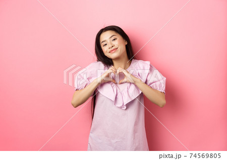 Valentines day concept. Beautiful korean teenager in dress showing heart gesture and smiling with admiration and affection, falling in love, feel romantic, pink background Valentines day concept. Beautiful korean teenager in dress showing heart gesture and smiling with admiration and affection, falling in love, feel romantic, pink background 74569805