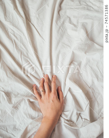 Woman's hand on background of crumpled bed sheet. Creased white linen. Woman touches unmade bed. Cozy imperfect house. Non-ideal cozy home. Woman's hand on background of crumpled bed sheet. Creased white linen. Woman touches unmade bed. Cozy imperfect house. Non-ideal cozy home. 74571386