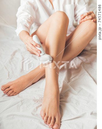 Woman takes care of herself, depilated legs with epilator. Epilation cosmetological procedure for hair removal. Spa at home. Skin care. Woman takes care of herself, depilated legs with epilator. Epilation cosmetological procedure for hair removal. Spa at home. Skin care. 74571486