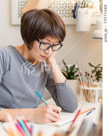 Woman with short hair cut is drawing in notebook. Calming hobby, anti stress leisure. Artist at work. Cozy workplace. Woman with short hair cut is drawing in notebook. Calming hobby, anti stress leisure. Artist at work. Cozy workplace. 74571488