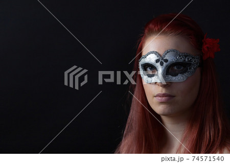 Portrait of redhead young woman posing with silver carnival mask 74571540