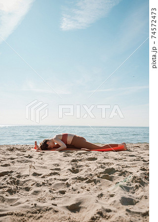 Young female in orange top and leggins practising Yoga split variation (Hanumanasana) on a beach in the morning Young female in orange top and leggins practising Yoga split variation (Hanumanasana) on a beach in the morning 74572473