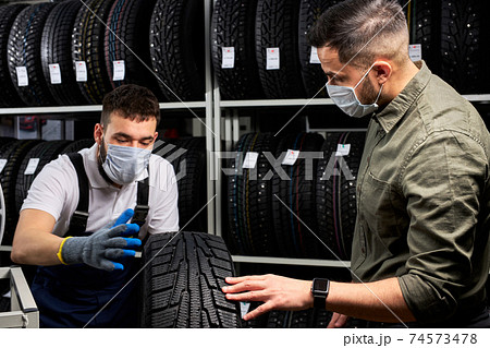 salesman and customer in medical mask stand discussing car tires salesman and customer in medical mask stand discussing car tires 74573478