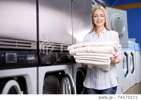 Young european caucasian woman with blond hair smiling happy doing chores at the laundry 74573571