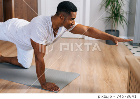 African-American man working out, doing stretching exercise on yoga mat while watching fitness video African-American man working out, doing stretching exercise on yoga mat while watching fitness video 74573641