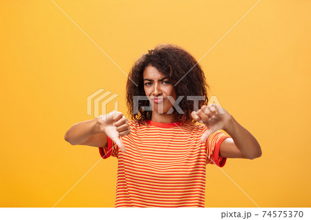 You loser and idea sucks. Dissatisfied and displeased young creative female artist with curly hairstyle frowning, sulking showing thumbd down in dislike gesture giving negative answer over orange wall You loser and idea sucks. Dissatisfied and displeased young creative female artist with curly hairstyle frowning, sulking showing thumbd down in dislike gesture giving negative answer over orange wall 74575370