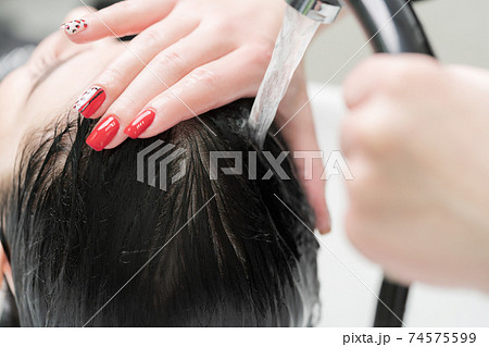 Hands of hairstylist wash hair of brunette with shampoo in professional sink for shampooing in beauty salon 74575599