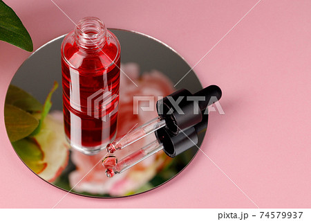 Glass bottle with oil on round mirror on pink background 74579937