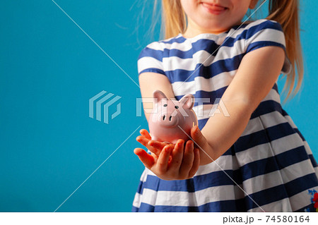 Little girl with piggy bank moneybox against blue background Little girl with piggy bank moneybox against blue background 74580164