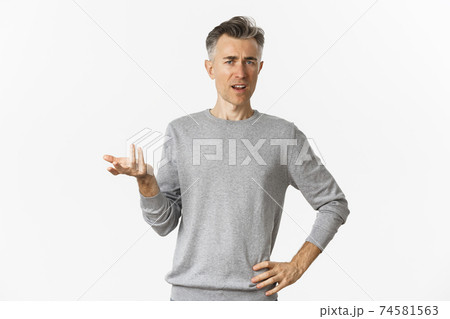 Portrait of confused and disappointed middle-aged man, pointing at something strange and looking at camera, waiting for explanation, standing over white background Portrait of confused and disappointed middle-aged man, pointing at something strange and looking at camera, waiting for explanation, standing over white background 74581563