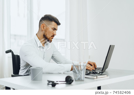 Serious concentrated man in wheelchair using his laptop for work / seeking a job in internet 74582406
