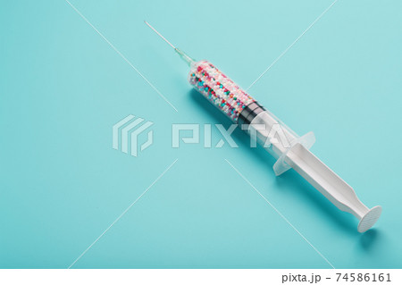 Syringe filled with colorful nano balls on a light blue background. 74586161