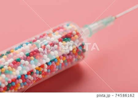 Medical Syringe filled with colorful balloons on a pink background with free space. 74586162