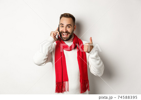 Handsome bearded man talking on phone, showing thumbs up in approval, like something, confirm order, standing over white background 74588395