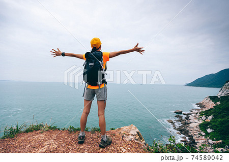 Successful hiker outstretched arms at seaside mountain top cliff edge Successful hiker outstretched arms at seaside mountain top cliff edge 74589042