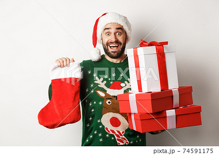 Xmas and winter holidays concept. Excited man holding christmas sock and gift boxes, celebrating New Year, bringing presents under tree, standing over white background 74591175