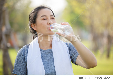 Asian elderly or senior woman drinking water in bottle after exercise for refreshing in garden,. 74591822