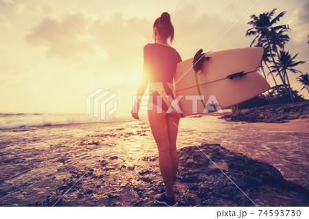 Female surfer walking with surfboard on the beach at sunrise Female surfer walking with surfboard on the beach at sunrise 74593730