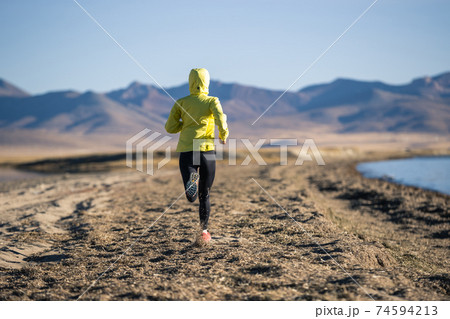 Woman trail runner cross country running on winter high altitude lakeside Woman trail runner cross country running on winter high altitude lakeside 74594213