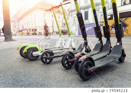 Many modern electric kick scooters sharing parked on city street. Self-service stree transport rental service. Rent urban mobility vehicle with smartphone application. Zero emission green eco energy. Many modern electric kick scooters sharing parked on city street. Self-service stree transport rental service. Rent urban mobility vehicle with smartphone application. Zero emission green eco energy. 74595213