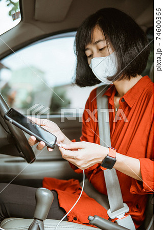 Woman in protective mask driving a car on road. charge phone Woman in protective mask driving a car on road. charge phone 74600366