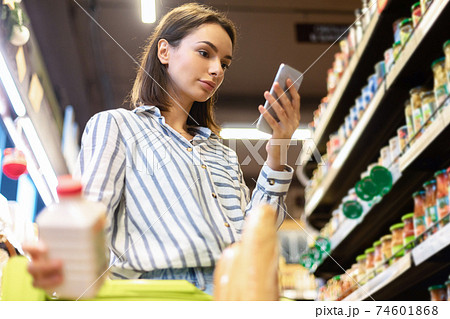 Lady holding smartphone standing in store taking products Lady holding smartphone standing in store taking products 74601868